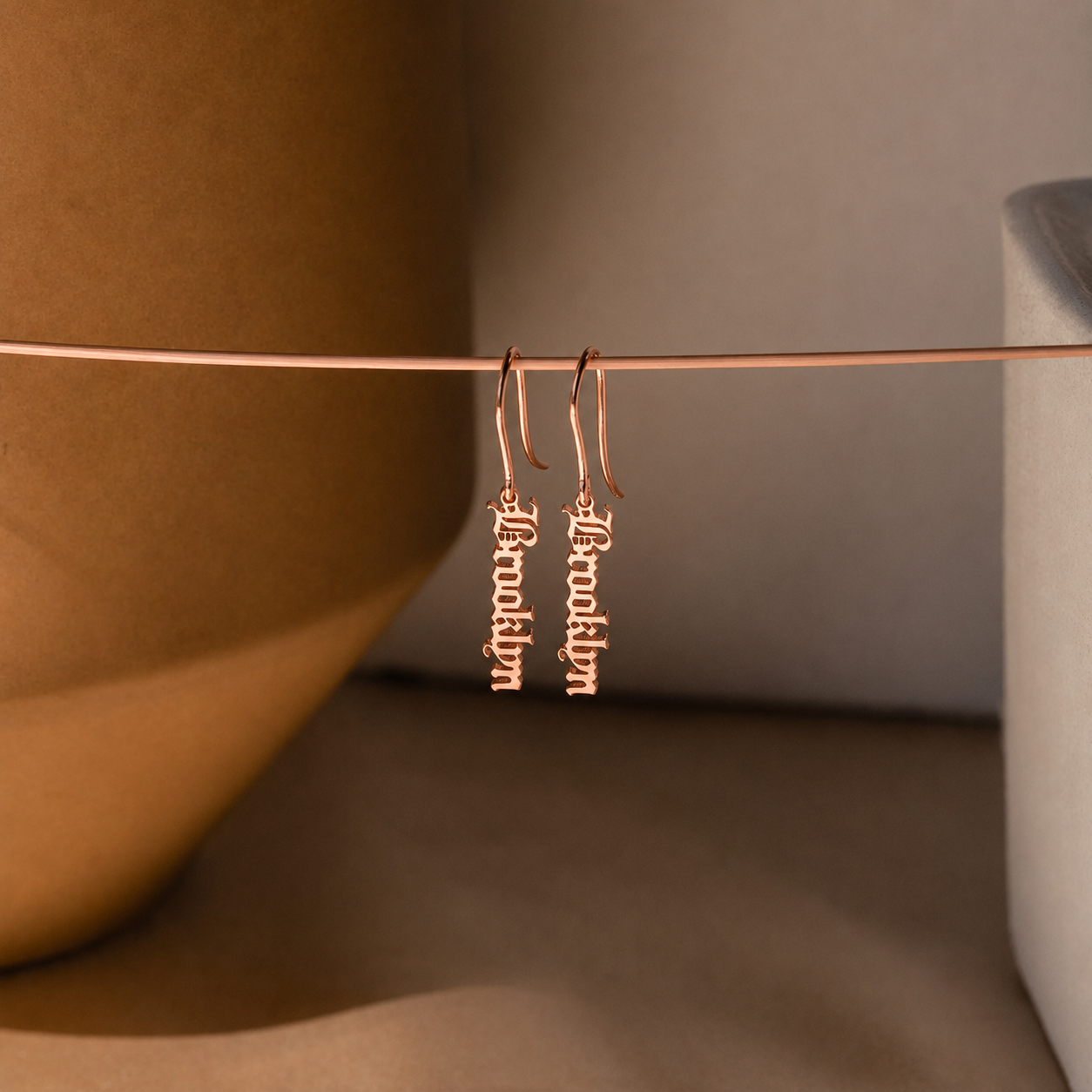 Rose gold earrings on a thin rod against a neutral background